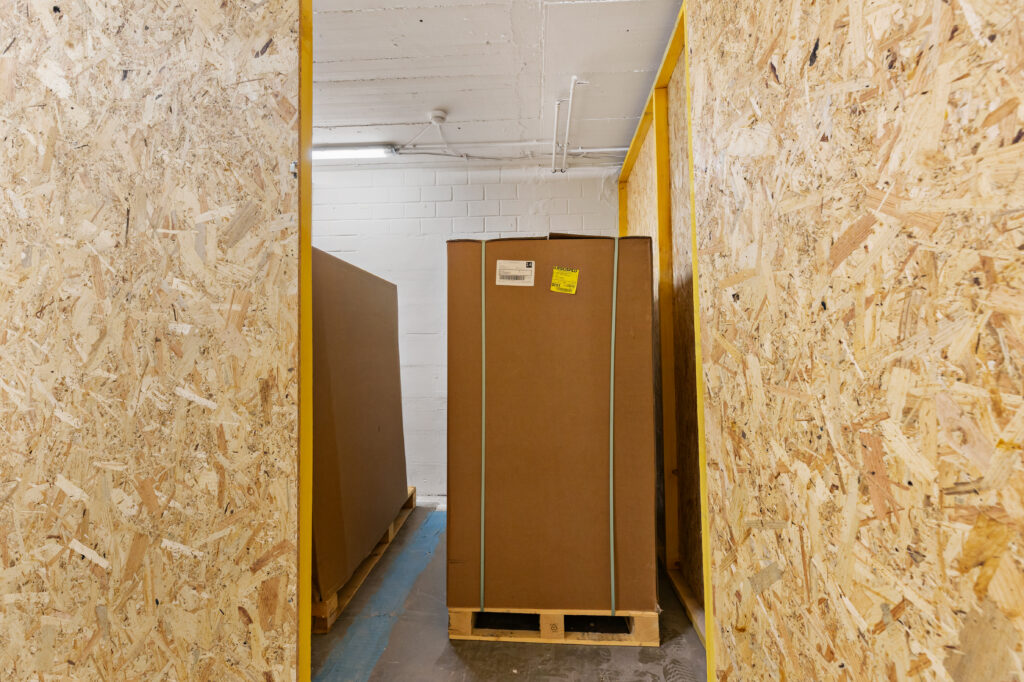 Box de garde-meuble Paladium au Luxembourg : carton stocké sur palette dans un box individuel sécurisé avec parois en OSB, accès 24h/7j, espace propre et ventilé pour le stockage de vos effets personnels, meubles et cartons.